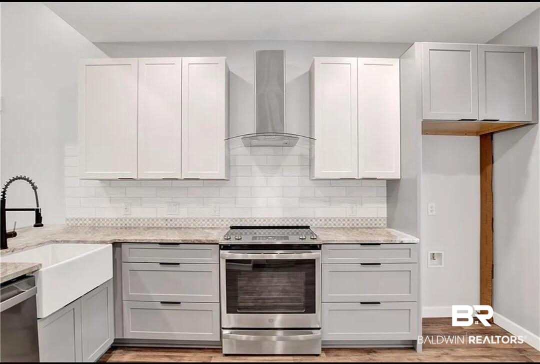 632 Ridgewood Drive Daphne, AL 36526 - Photo 10 of 36 Kitchen with sink, light stone counters, stainless steel appliances, wall chimney range hood, and light wood-type flooring