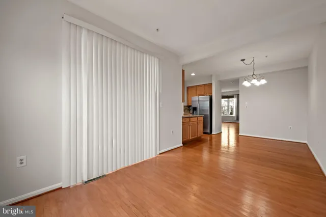 a view of an empty room with wooden floor and a kitchen