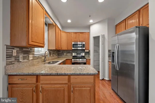 a kitchen with stainless steel appliances granite countertop a refrigerator a stove and a sink with wooden cabinets