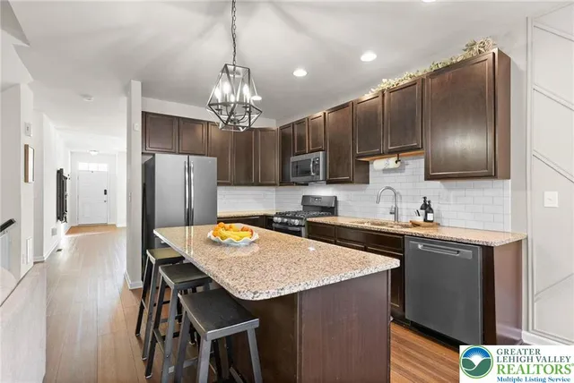 a kitchen with stainless steel appliances granite countertop a refrigerator a sink dishwasher a stove and a wooden floor