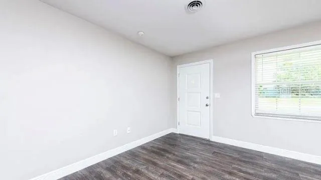 a view of an empty room with wooden floor and a window