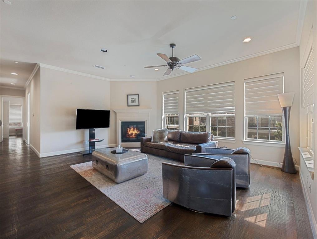 5001 Meridian Lane, Unit 2103 Addison, TX 75001 - Photo 3 of 26 Spacious living area featuring dark wood-finish flooring, a corner fireplace with a mantel, multiple windows with blinds, crown molding, and recessed lighting