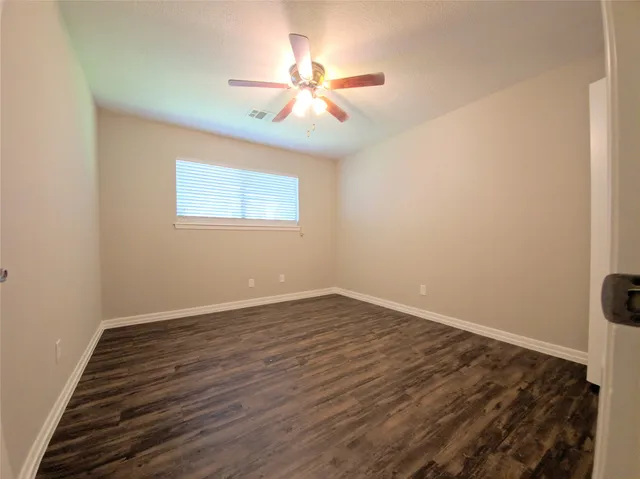 an empty room with wooden floor fan and windows