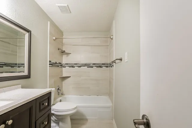 a bathroom with a granite countertop bathtub shower sink vanity and toilet
