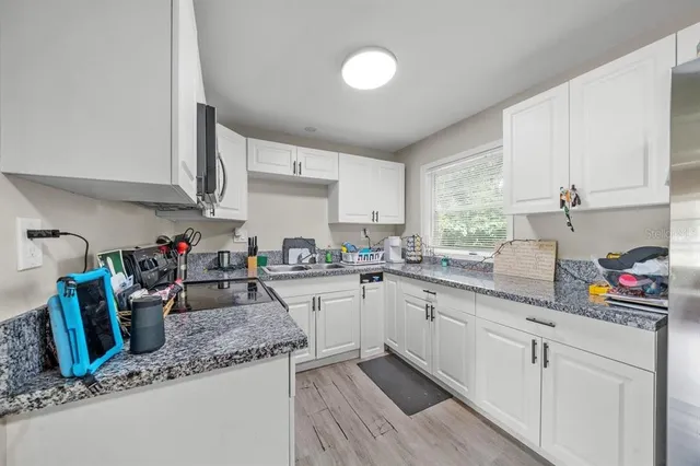 a kitchen with granite countertop a sink a stove top oven a counter space and cabinets