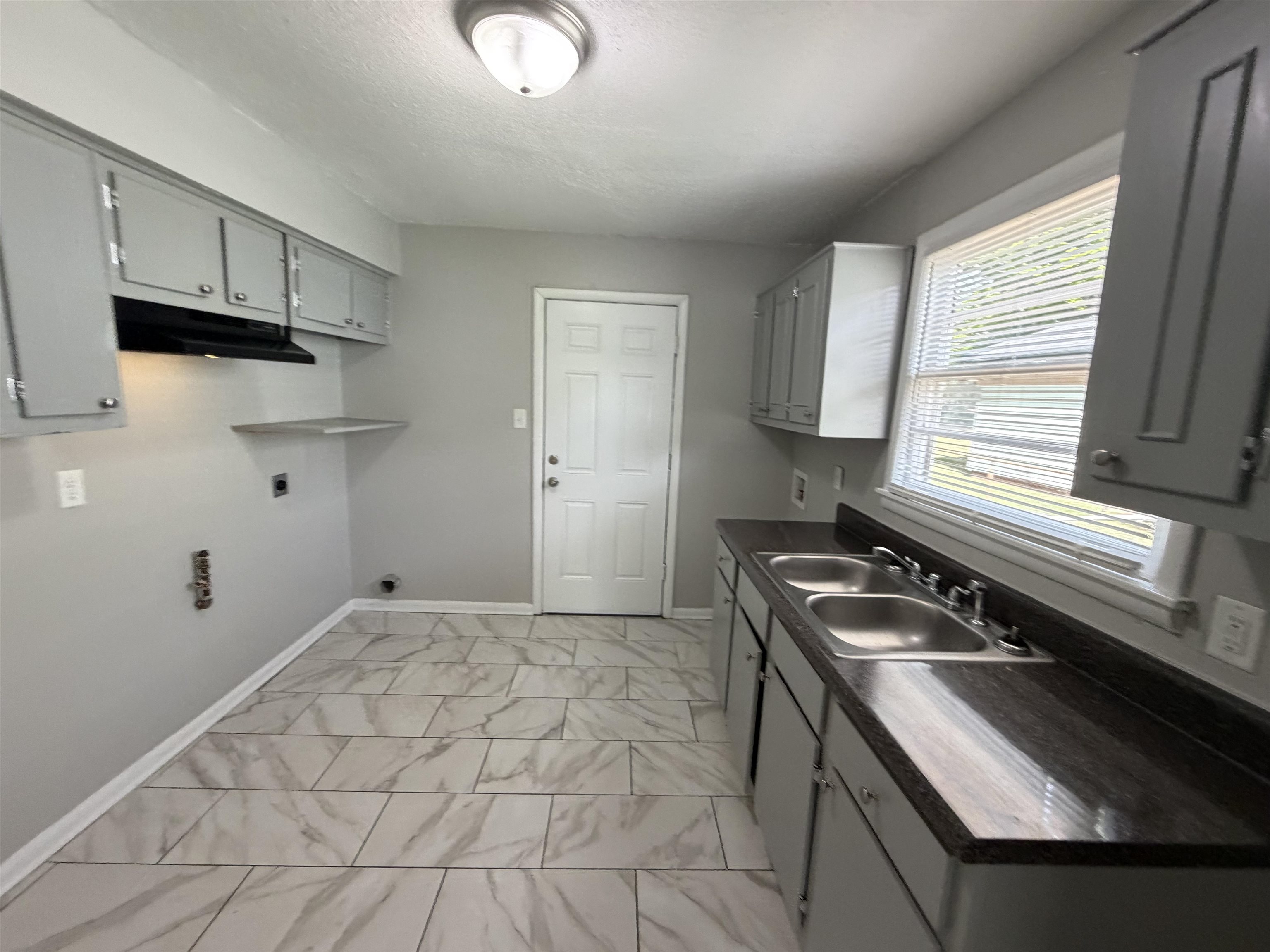 3525 Rochester Road Memphis, TN 38109 - Photo 5 of 10 Kitchen area featuring grey cabinetry with silver-tone hardware, a double basin stainless steel sink, and dark countertops