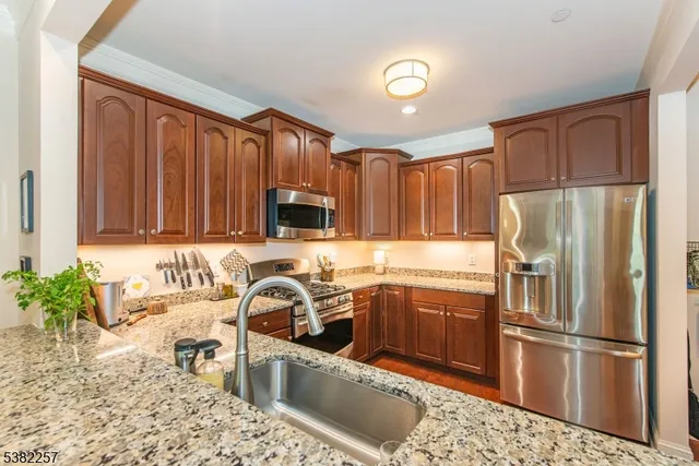 a kitchen with stainless steel appliances granite countertop a refrigerator a sink dishwasher a stove with wooden cabinets and floor