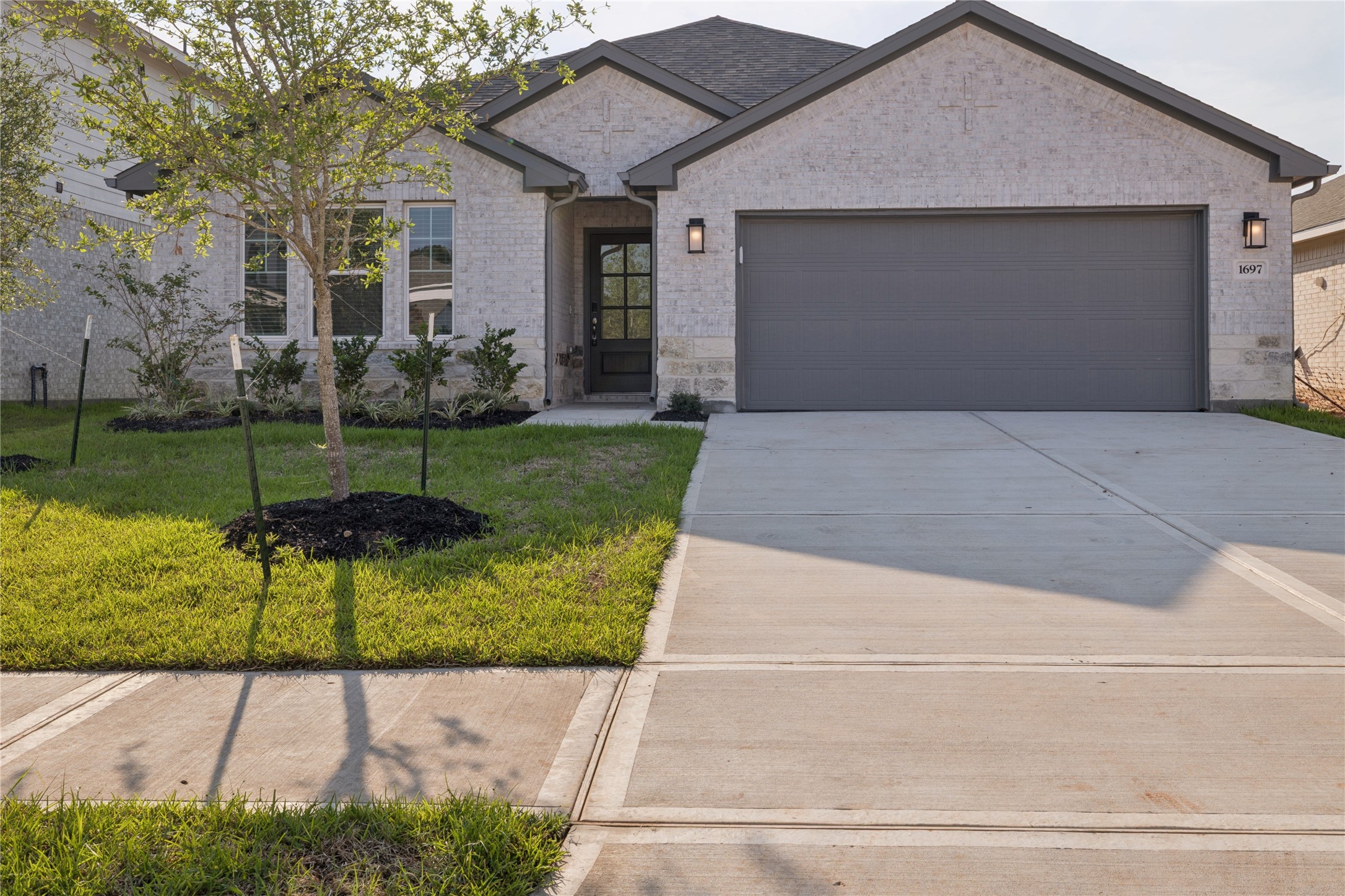 Charming modern home with a light brick exterior, spacious two-car garage, and a welcoming front entryway framed by lush greenery.