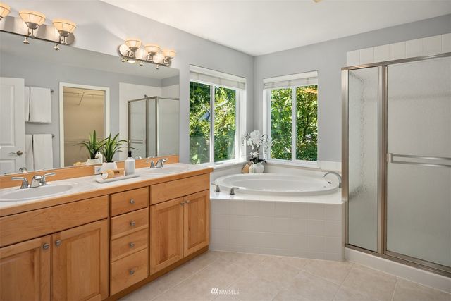 a bathroom with a double vanity sink a large mirror a bathtub and next to a window
