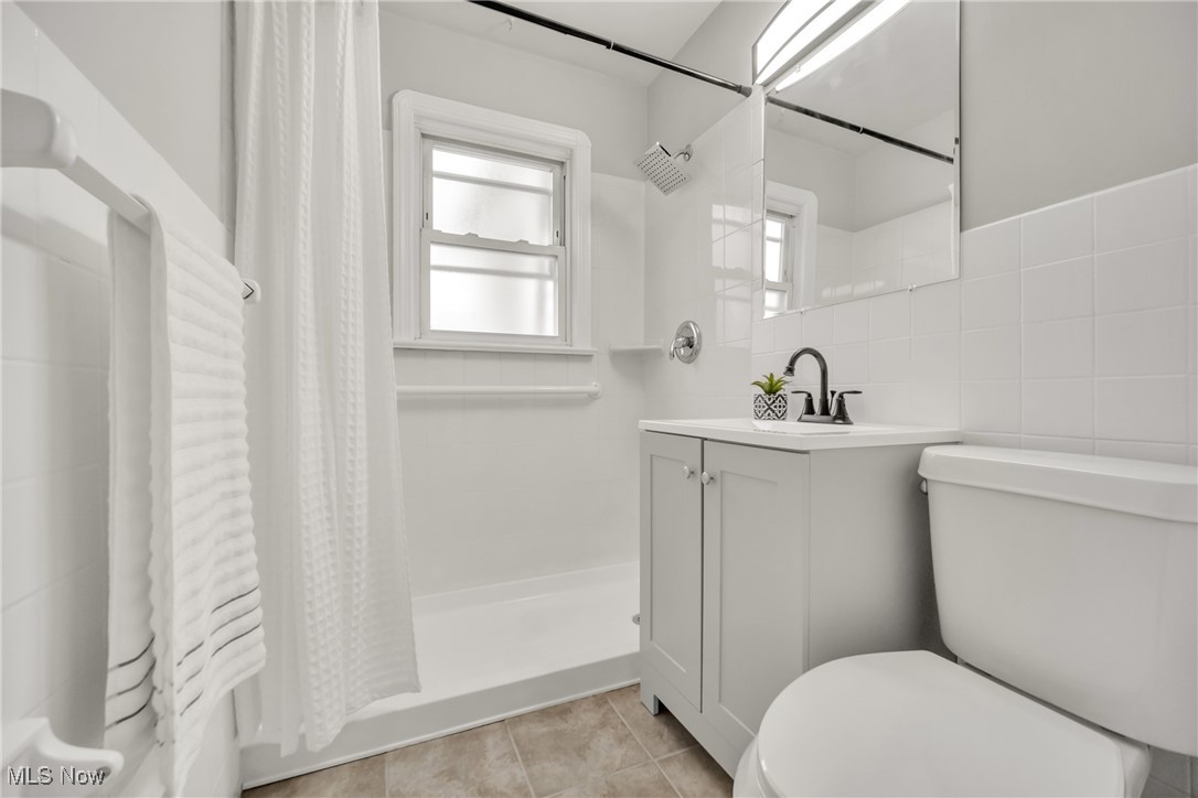 12910 Rockside Road Cleveland, OH 44125 - Photo 13 of 34 Bathroom with tile patterned floors, toilet, vanity, a shower with shower curtain, and tile walls