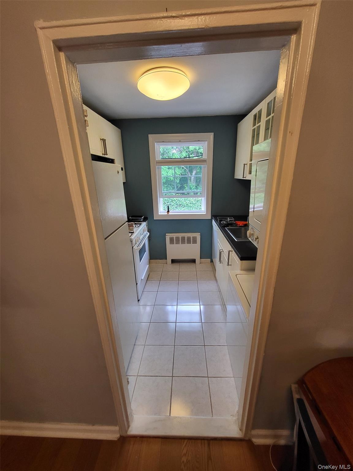 224-23 Kingsbury Avenue, Unit B Queens, NY 11364 - Photo 14 of 22 Kitchen with radiator heating unit, dark countertops, white cabinetry, and white appliances