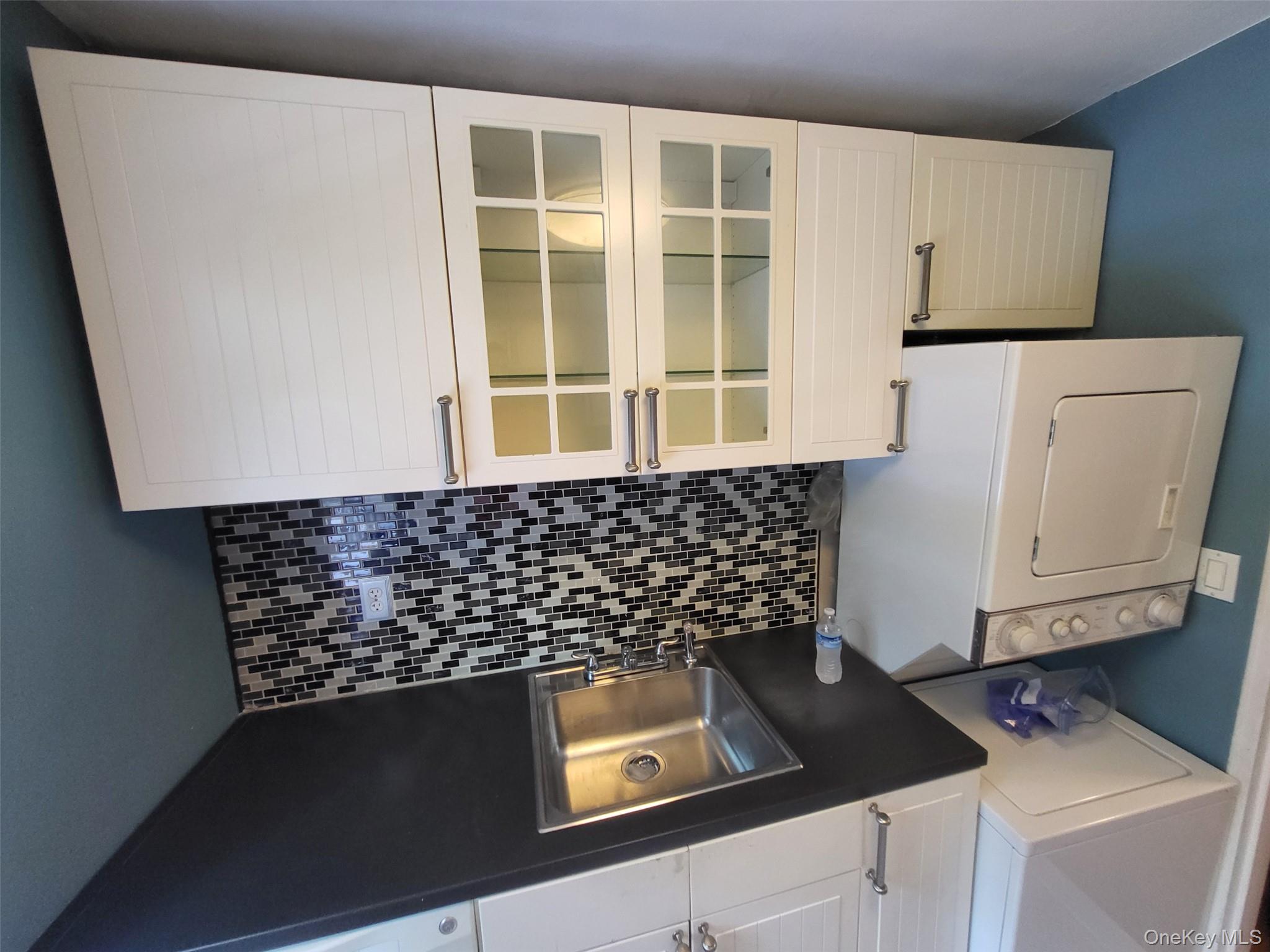 224-23 Kingsbury Avenue, Unit B Queens, NY 11364 - Photo 18 of 22 Kitchen with dark countertops, stacked washing machine and dryer, tasteful backsplash, and white cabinetry