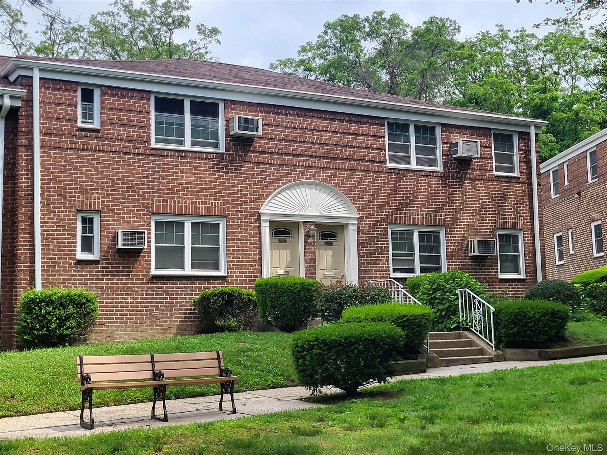 224-23 Kingsbury Avenue, Unit B Queens, NY 11364 - Photo 4 of 22 View of front facade featuring an AC wall unit, brick siding, and a front lawn