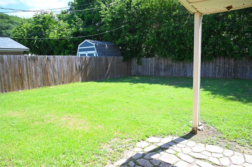 1352 Simpson Drive Hurst, TX 76053 - Photo 20 of 40 Private backyard with wood privacy fencing, a storage shed, and a stone-paver patio area