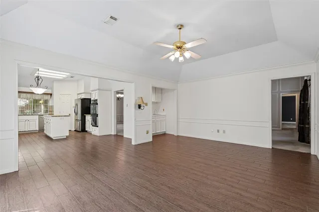 a view of an empty room with wooden floor and kitchen view