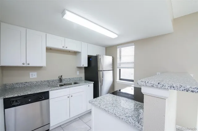 a kitchen with granite countertop a refrigerator and white cabinets