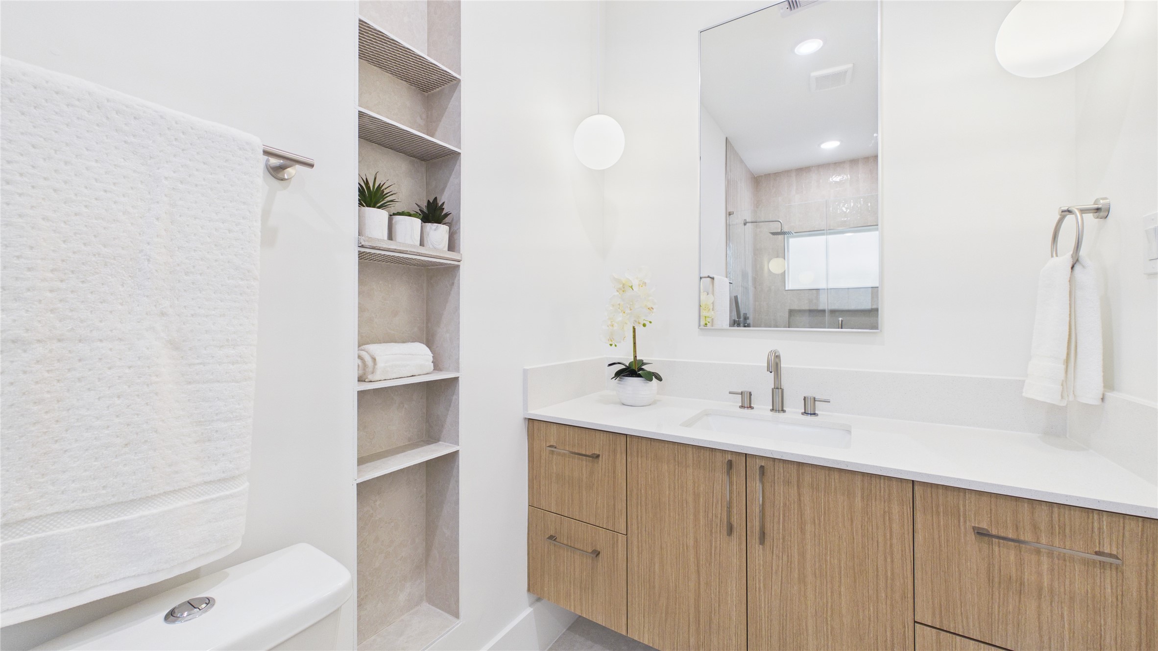 602 Skyland Terrace Way Houston, TX 77009 - Photo 9 of 40 Modern bathroom with a sleek design featuring a large mirror, wooden vanity with dual sinks, and open shelving for storage. Bright and inviting with white walls and contemporary fixtures.