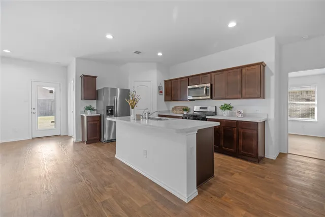 a kitchen with stainless steel appliances a microwave a sink a stove a refrigerator cabinets and wooden floor