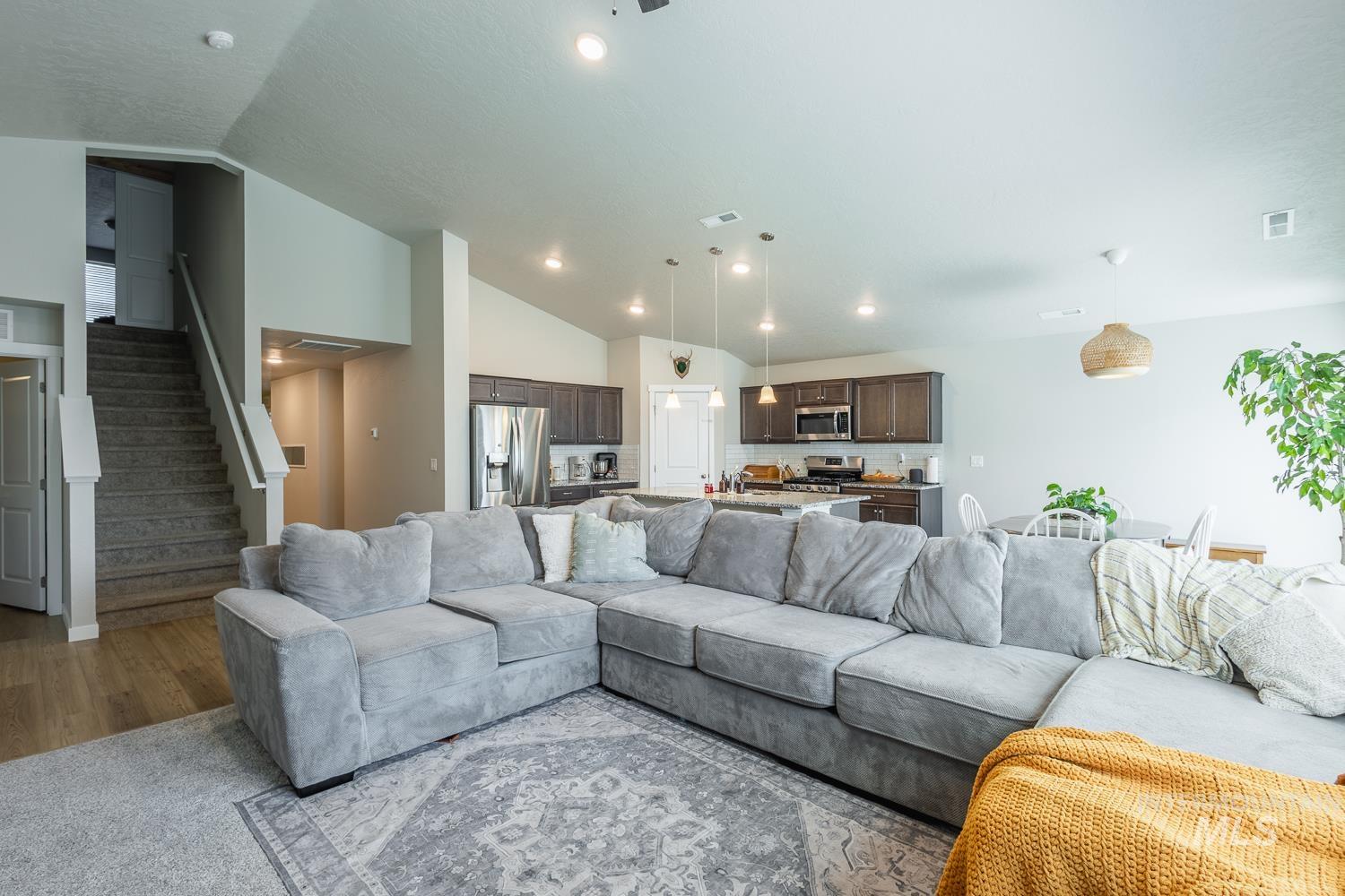12623 Shadow Peak Street Caldwell, ID 83607 - Photo 11 of 50 Open-concept living space featuring wood-finish flooring, a carpeted staircase, and a kitchen with stainless steel appliances and dark wood cabinetry