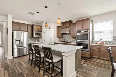 a kitchen with stainless steel appliances kitchen island granite countertop a table chairs stove and refrigerator