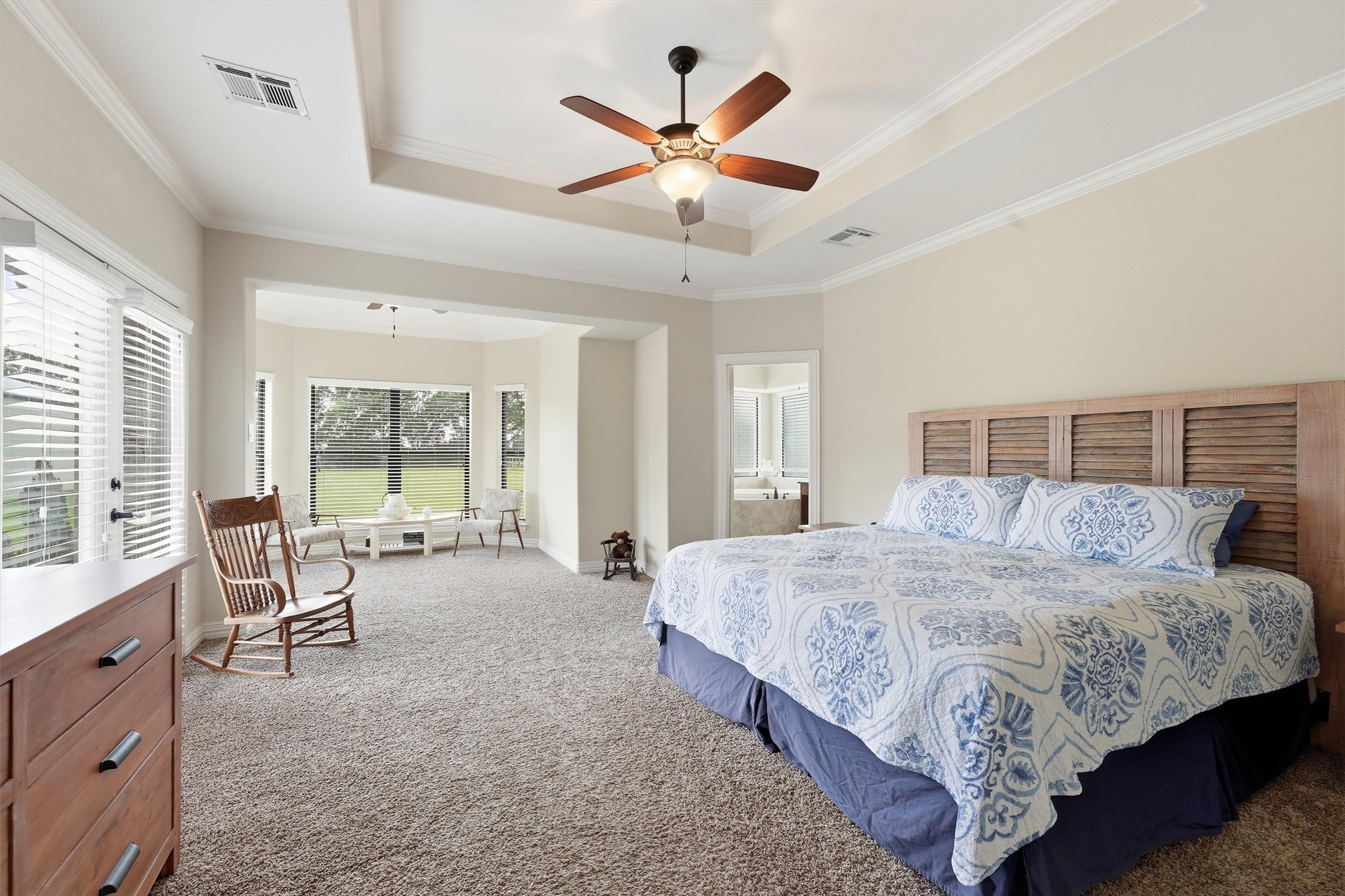 4810 Magnolia Bend Drive Rosharon, TX 77583 - Photo 16 of 40 Spacious primary bedroom featuring a cozy sitting area with large windows, tray ceiling, plush carpeting, and a ceiling fan for comfort.