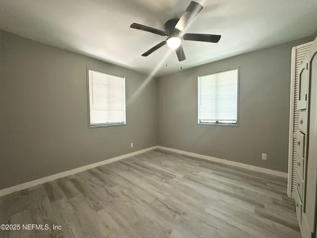 an empty room with wooden floor ceiling fan and windows