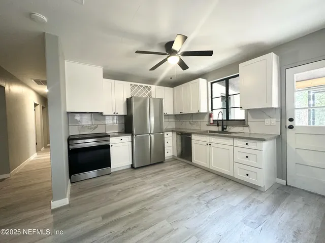 a kitchen with granite countertop a refrigerator oven a sink and white cabinets