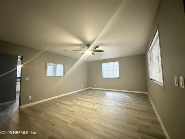 an empty room with wooden floor windows and ceiling fan