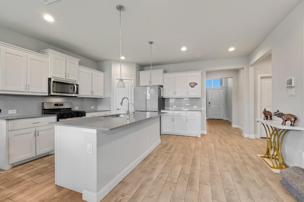 1112 Croxley Way Justin, TX 76247 - Photo 4 of 18 Modern kitchen featuring a central island with a sink, stainless steel appliances, white cabinetry, a gray subway tile backsplash, and wood-finish flooring