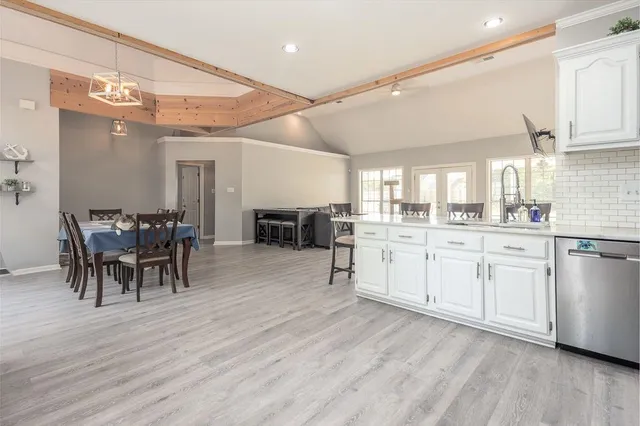 a large white kitchen with granite countertop a stove a sink a dining table and chairs with wooden floor