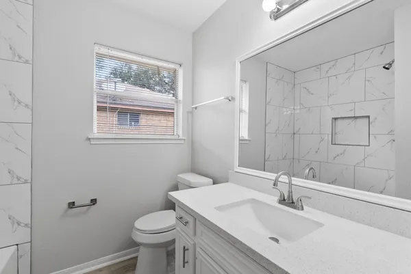 a bathroom with a granite countertop toilet a sink a mirror a window and vanity