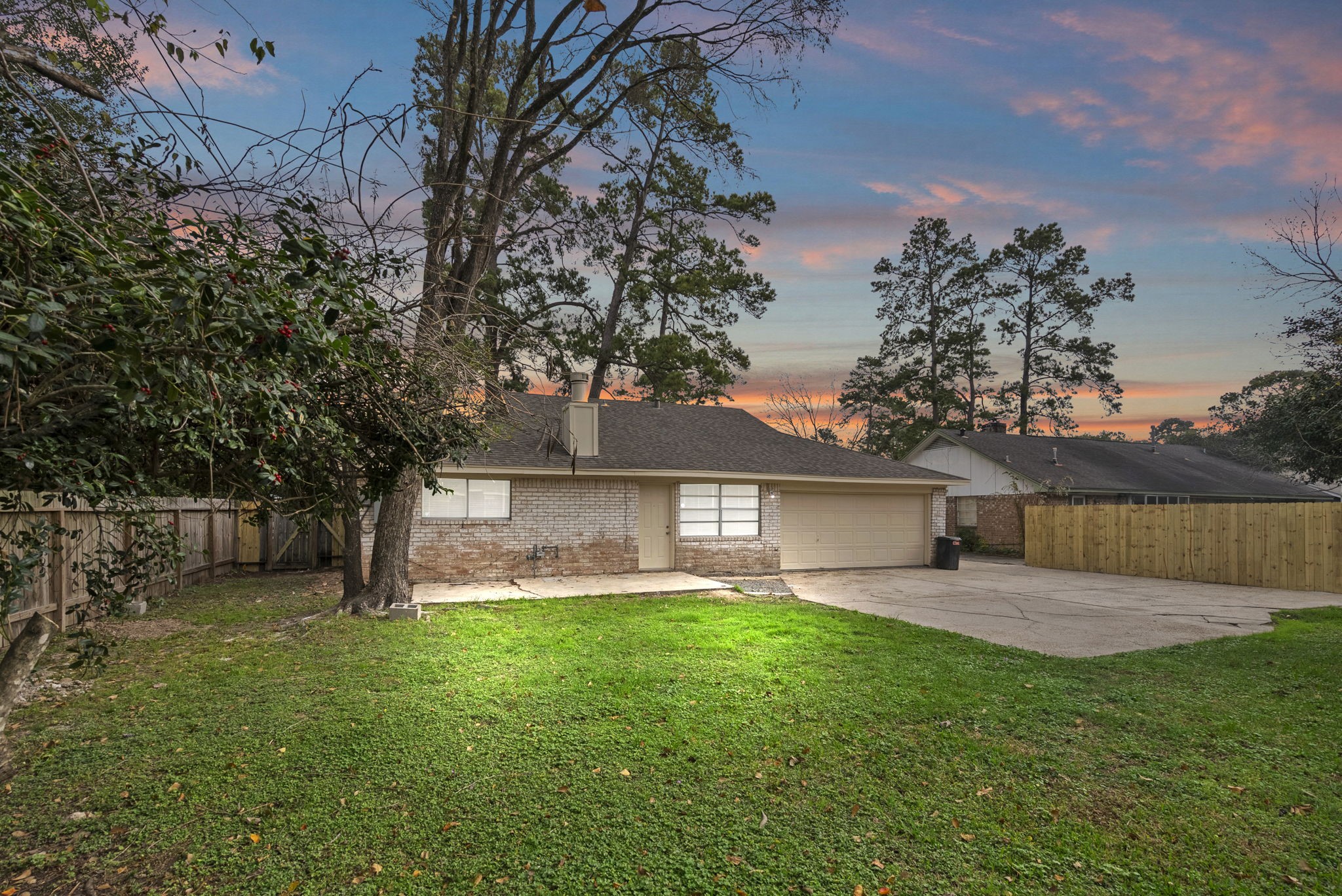 23111 Canyon Lake Drive Spring, TX 77373 - Photo 20 of 24 Back view of the home showing brick exterior, attached two-car garage, and large driveway area extending into the backyard. Spacious fenced yard offers open lawn space with mature trees along the property line.