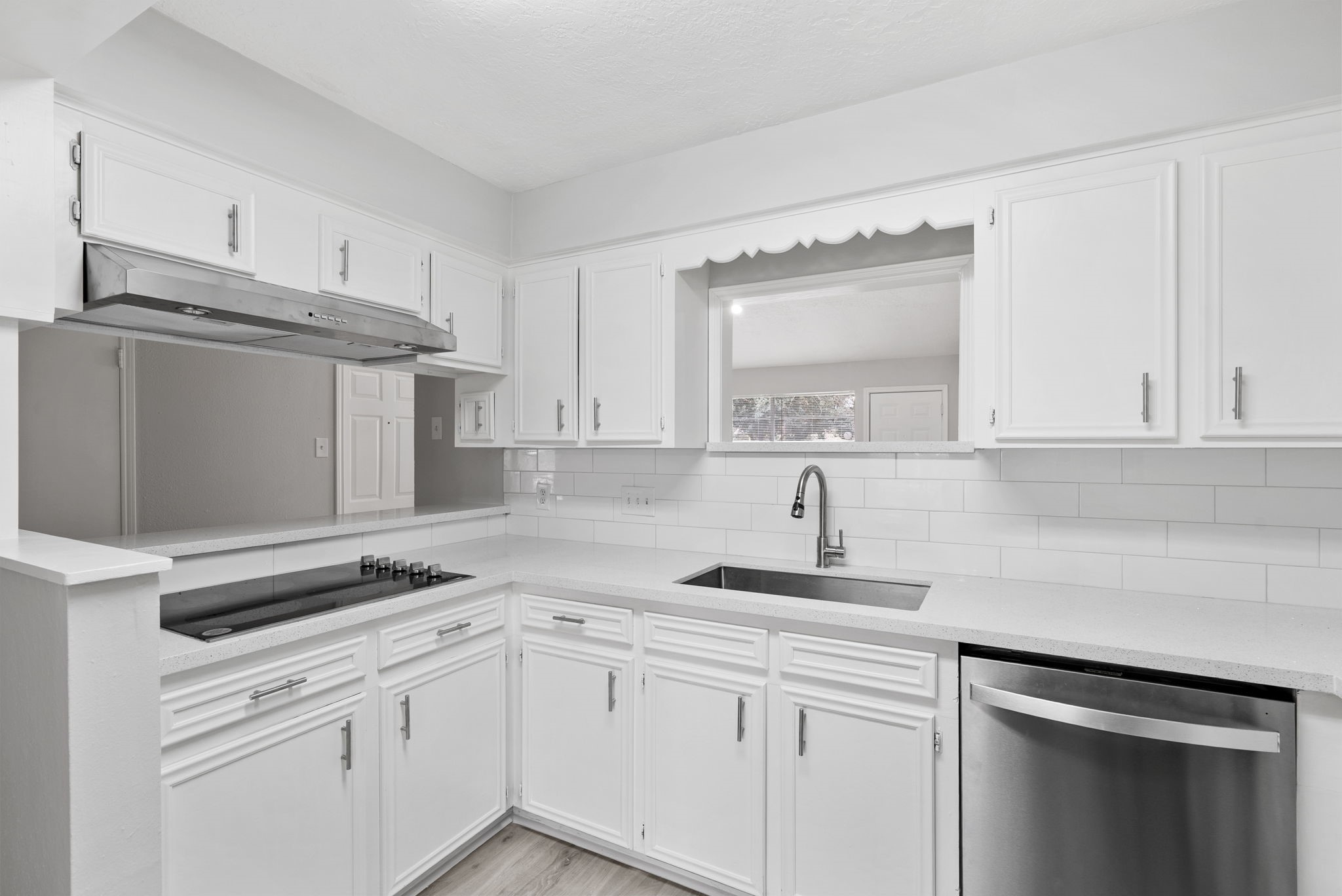 23111 Canyon Lake Drive Spring, TX 77373 - Photo 9 of 24 Kitchen with white cabinetry, subway tile backsplash, and solid-surface countertops. U-shaped work area includes electric cooktop with vent hood, stainless steel appliances and pass-through opening to the living room.
