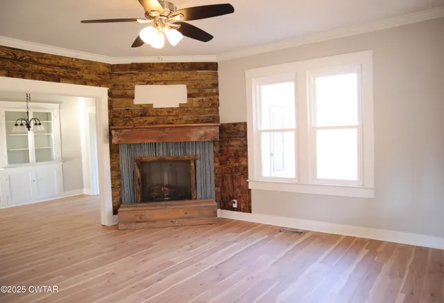 a view of an empty room with wooden floor fireplace and a window