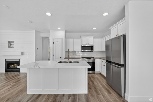14771 Haddington Road Draper, UT 84020 - Photo 12 of 44 Kitchen featuring a large island with sink, stainless steel appliances, white cabinetry, and wood-finish flooring