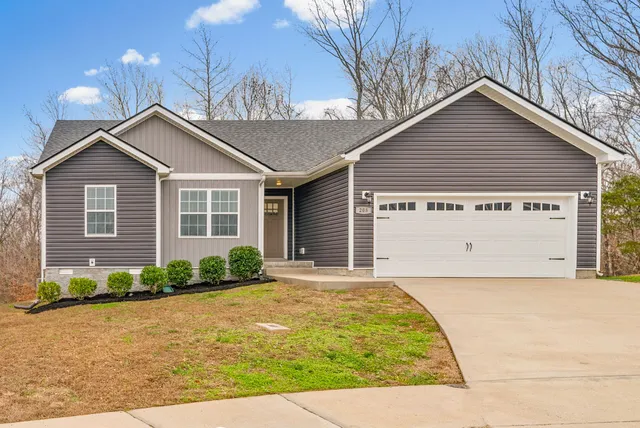 a view of a house with a yard plants and large tree