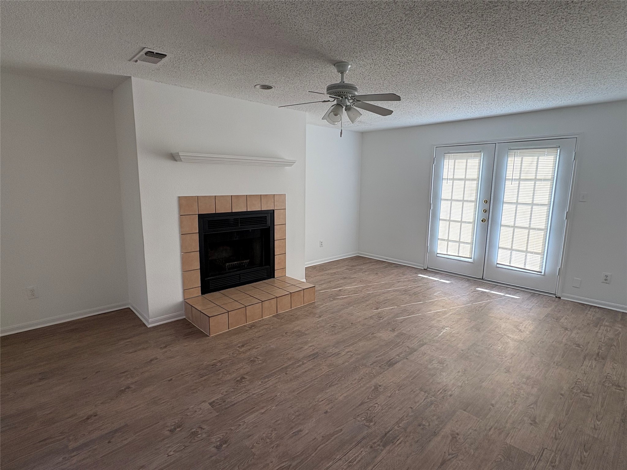 9201 Simmons Road, Unit 119 Austin, TX 78759 - Photo 5 of 22 Unfurnished living room with french doors, a ceiling fan, wood finished floors, a fireplace, and a textured ceiling