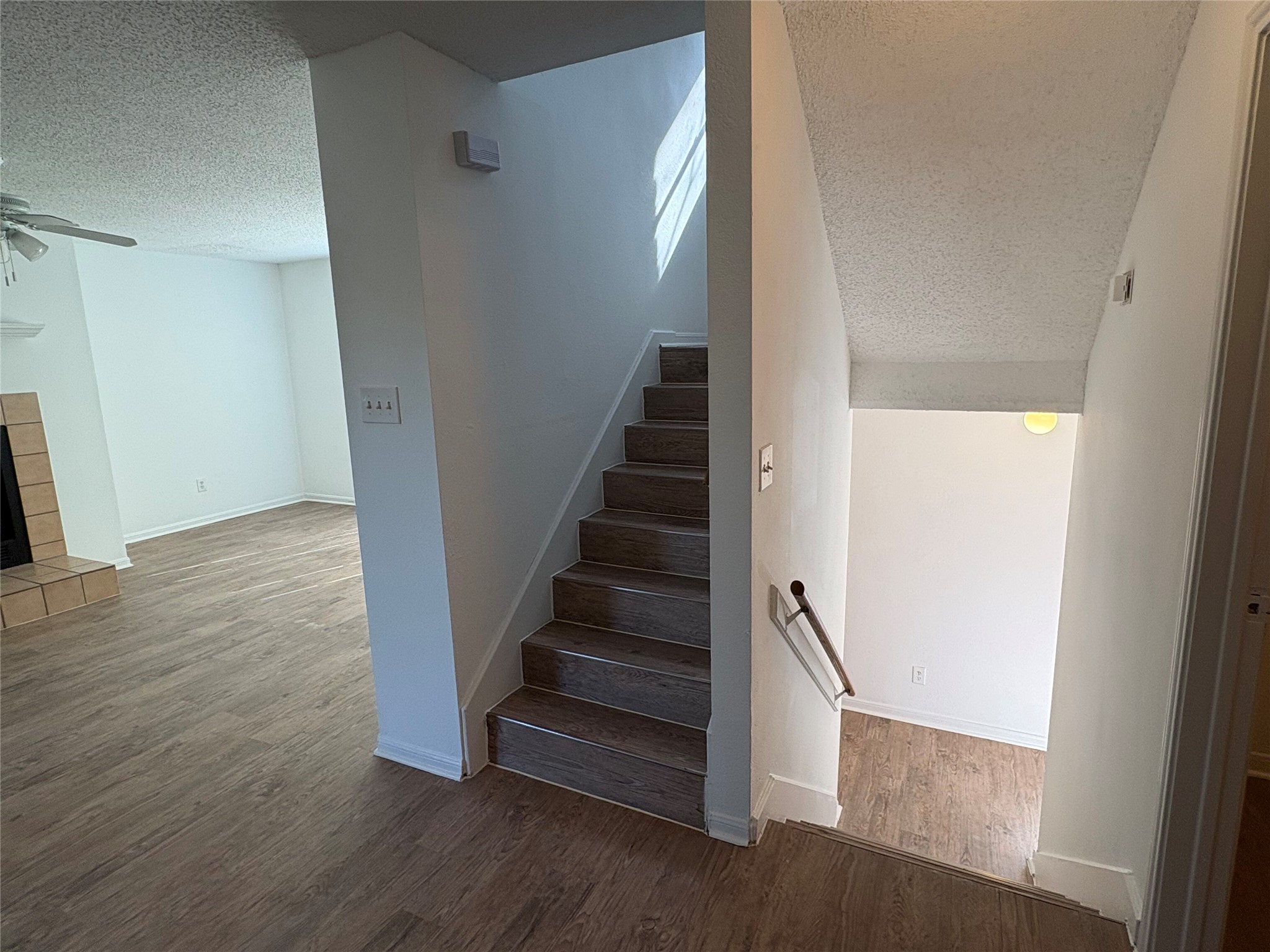 9201 Simmons Road, Unit 119 Austin, TX 78759 - Photo 6 of 22 Staircase featuring a textured ceiling, wood finished floors, ceiling fan, and a fireplace