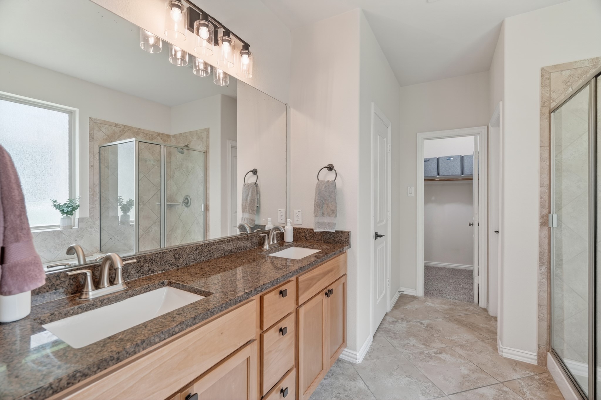 79 West Jagged Ridge Circle Spring, TX 77389 - Photo 25 of 50 This view of the primary bathroom showcases the glass-enclosed shower, additional vanity space, and a window that brings in natural light. The neutral tile and warm cabinetry combine for a timeless, spa-like feel in this private retreat.