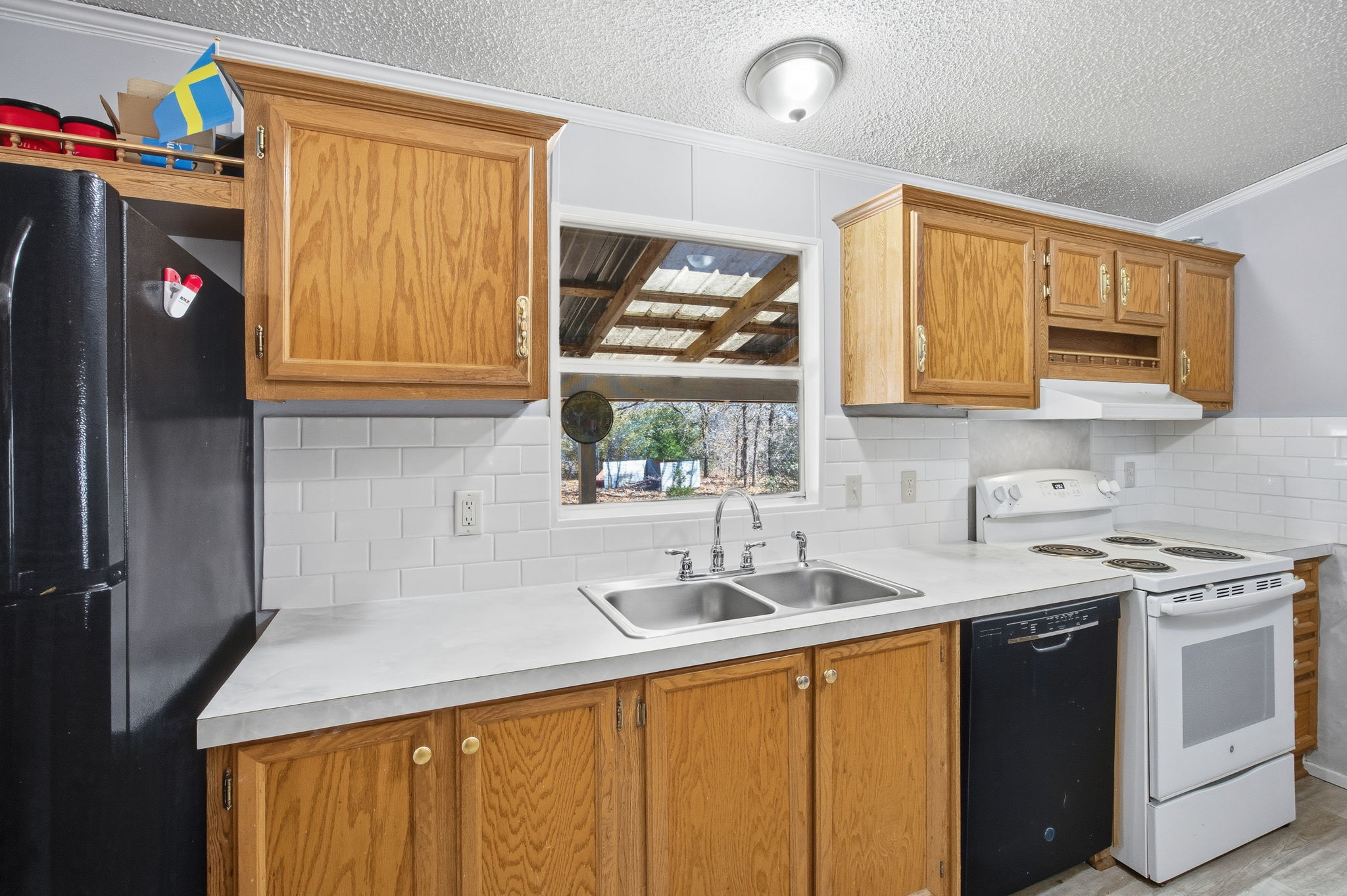 182 Wayside Court Elgin, TX 78621 - Photo 12 of 40 Kitchen with crown molding, black appliances, light countertops, a textured ceiling, and wood finish cabinets