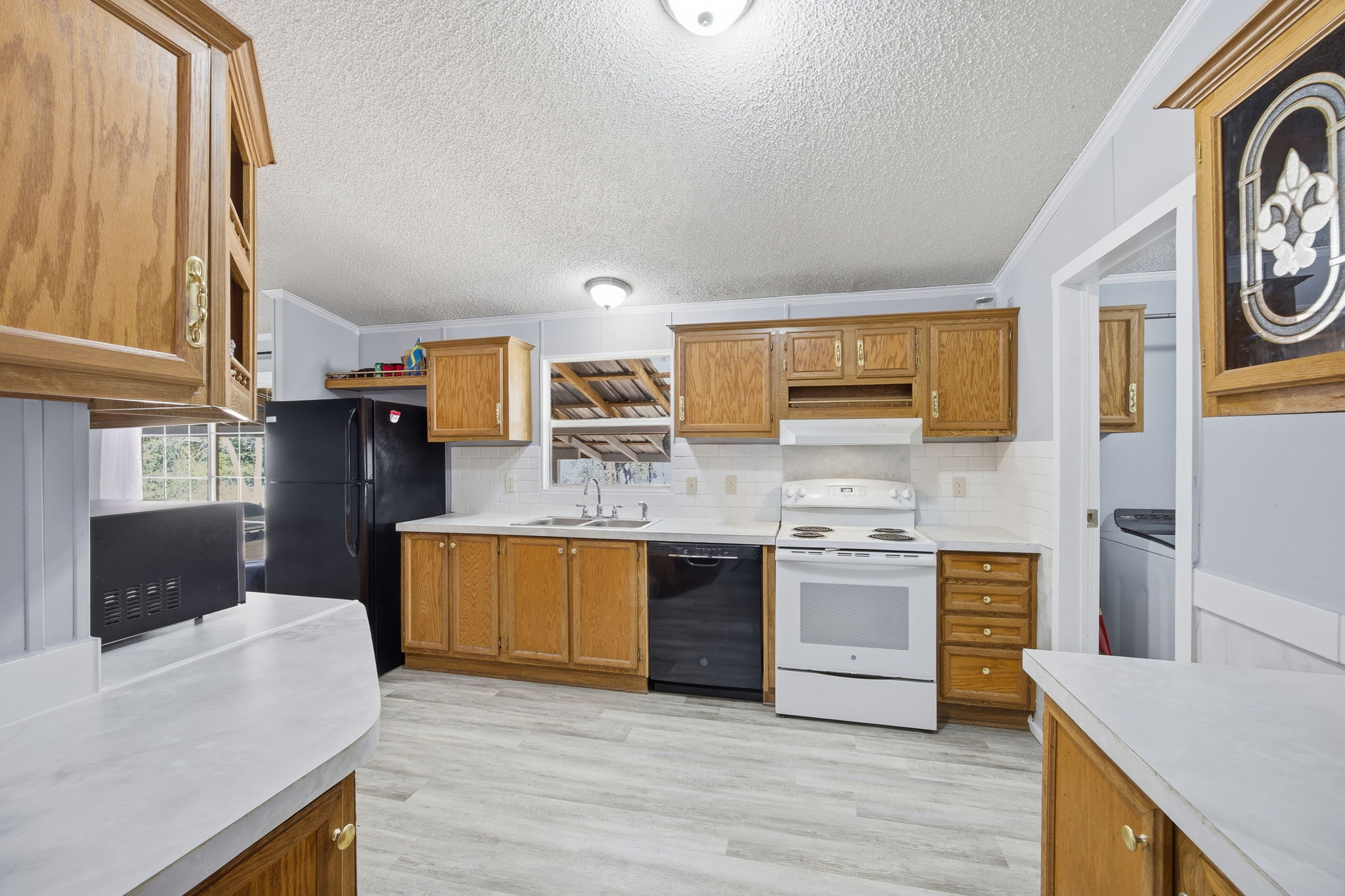 182 Wayside Court Elgin, TX 78621 - Photo 14 of 40 Kitchen featuring ornamental molding, wood finish cabinetry, black appliances, light countertops, and tasteful backsplash