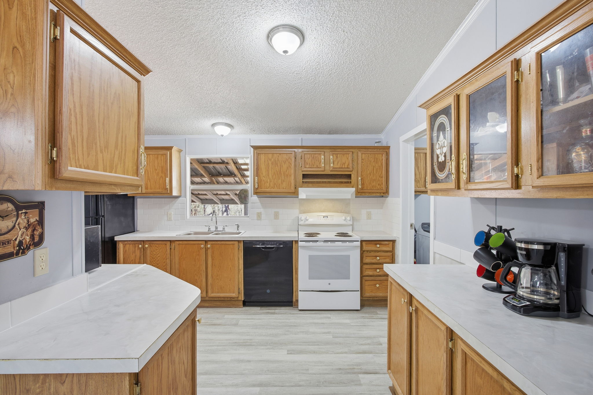 182 Wayside Court Elgin, TX 78621 - Photo 16 of 40 Kitchen featuring light countertops, wood finish cabinets, black appliances, a textured ceiling, and backsplash