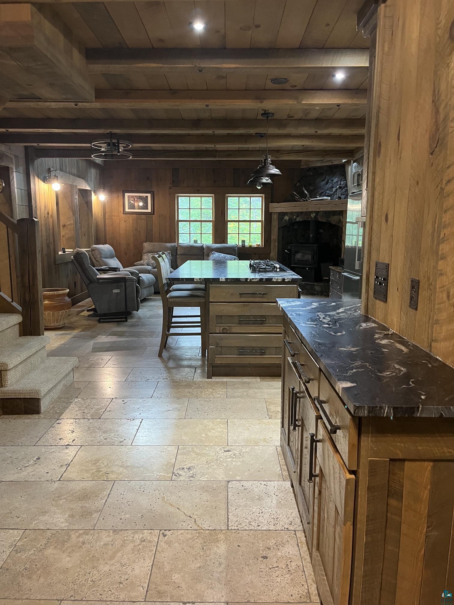 70745 Range Line Road Iron River, WI 54847 - Photo 8 of 40 Travertine tile flooring, wood-paneled walls, exposed wood beam ceiling, wood-finish cabinetry with dark countertops, and a stone-clad fireplace