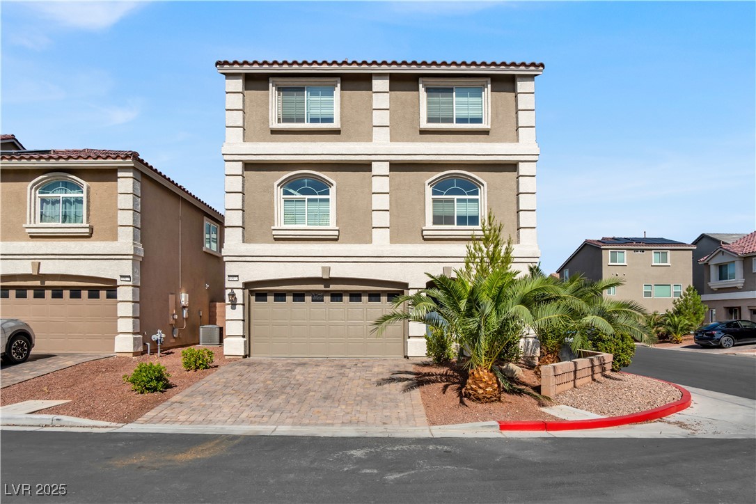 Townhome / multi-family property with a garage, stucco siding, and decorative driveway