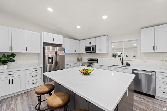 Kitchen with light stone counters, stainless steel appliances, a kitchen island, light wood-style floors, and lofted ceiling