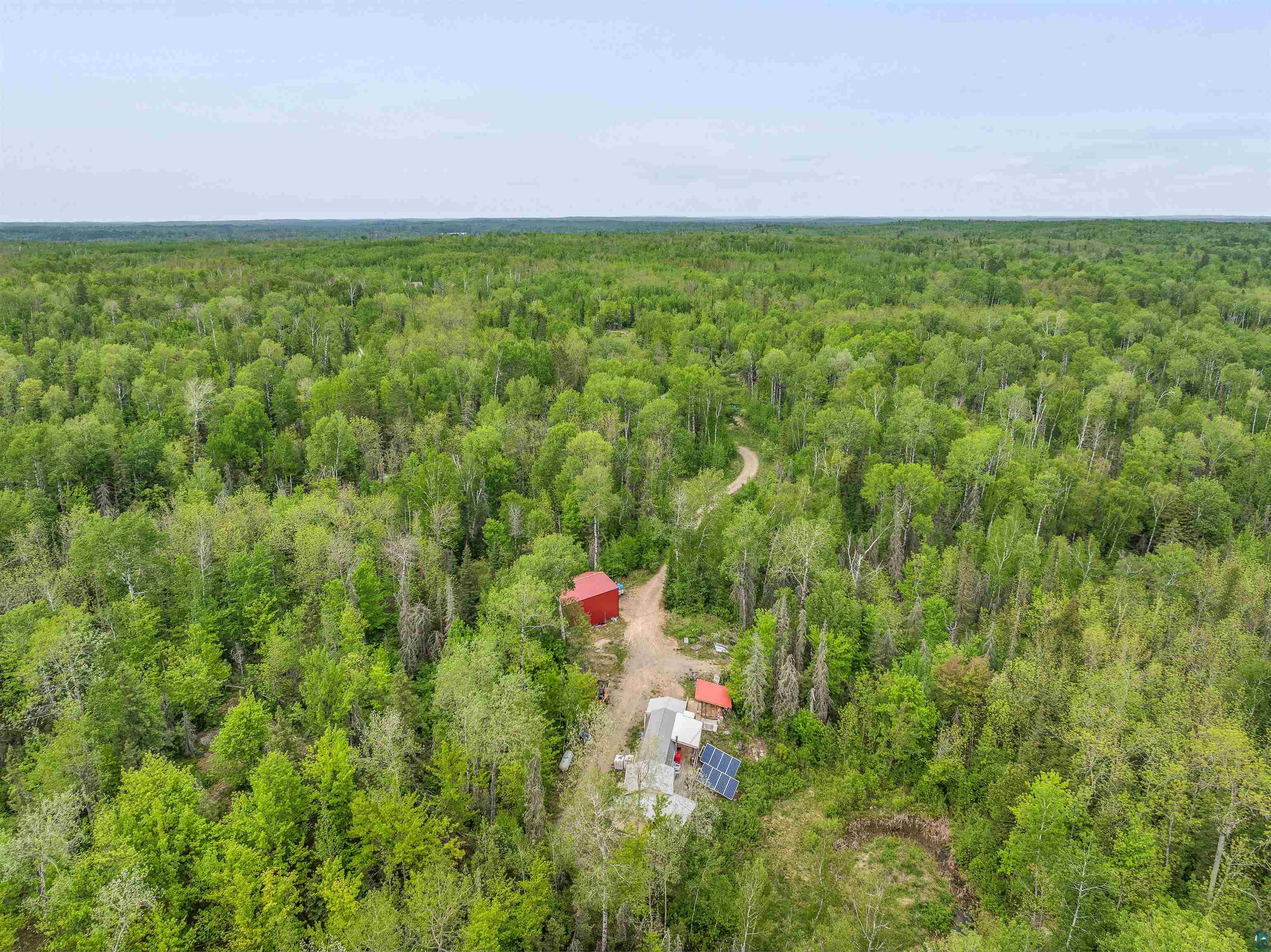 1152 Fernberg Road Ely, MN 55731 - Photo 9 of 24 Extensive wooded acreage featuring a red outbuilding, an additional structure with solar panels, and a winding dirt road
