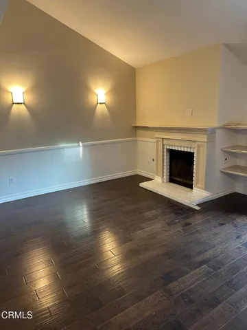 an empty room with wooden floor fireplace and windows