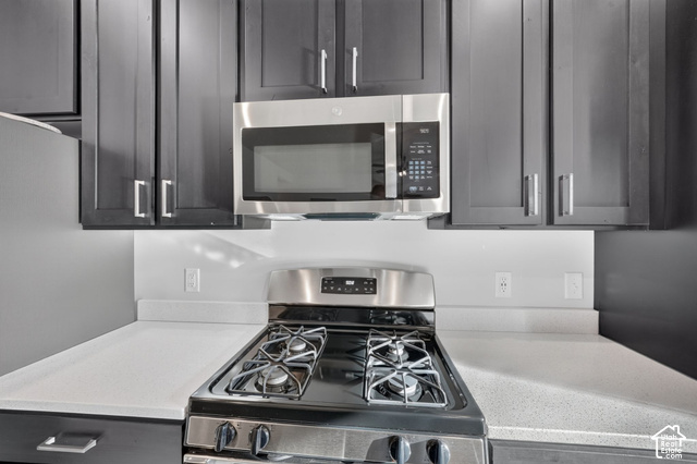 1081 Bowery Way Mapleton, UT 84664 - Photo 7 of 41 Stainless steel gas range, built-in stainless steel microwave, light-toned countertop, and dark cabinetry