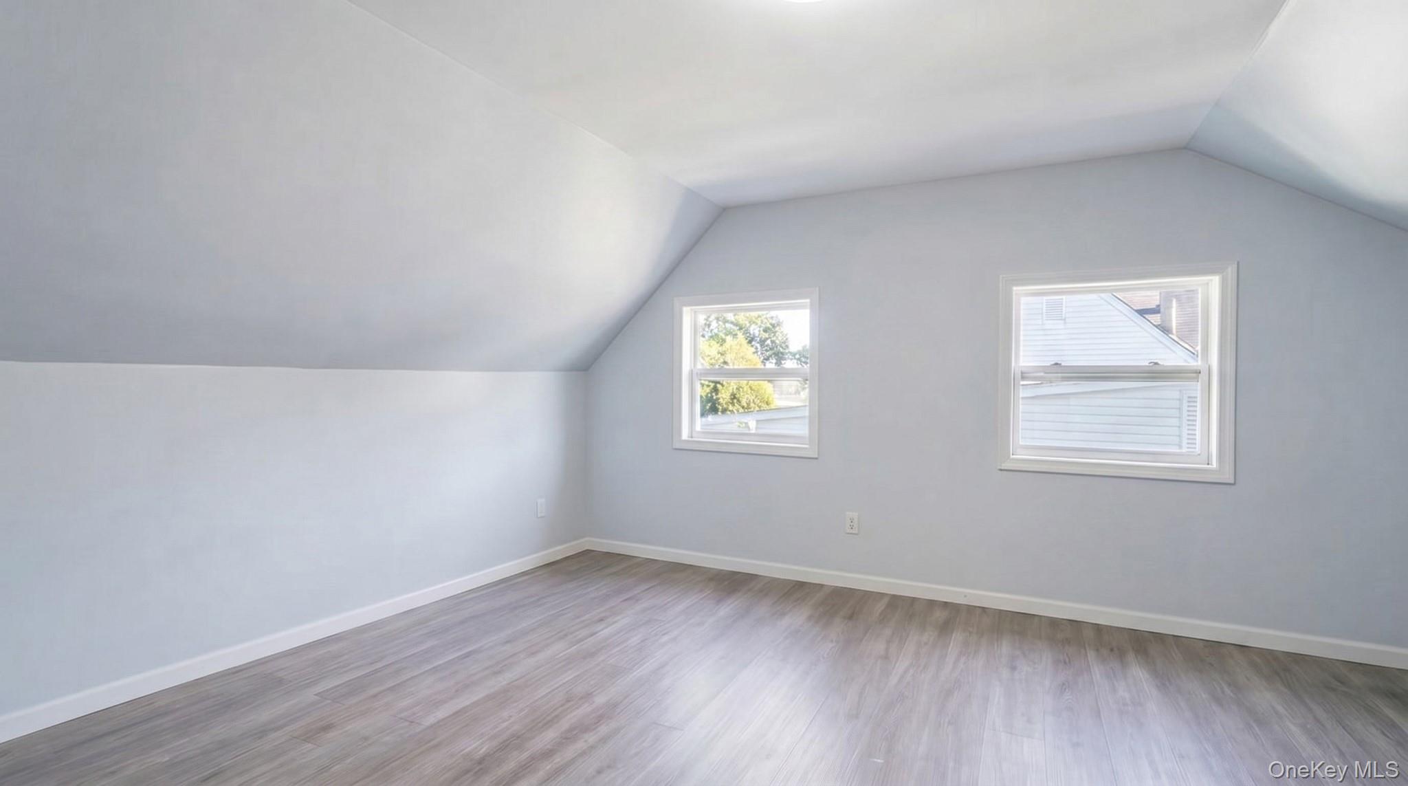 63 Blacksmith Road Levittown, NY 11756 - Photo 20 of 25 Attic room with wood-finish flooring, two windows, vaulted ceiling, and light-toned wall finishes