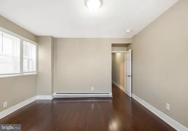 an empty room with wooden floor and windows with curtains